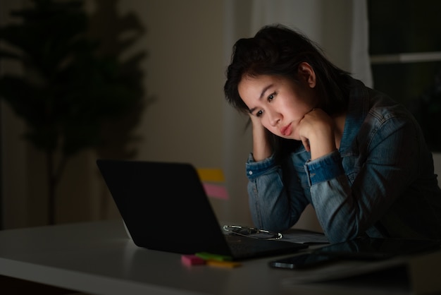 A women sits at a computer contemplating the words on the screen with her head slightly tilted to the left Late night computer